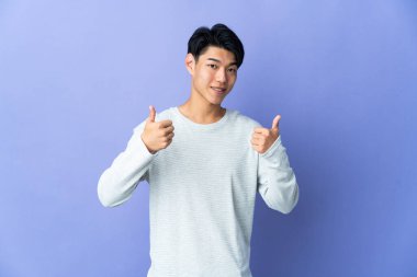 Mor arka planda izole edilmiş genç bir Çinli baş parmak hareketi yapıyor.