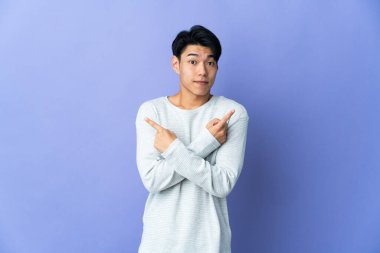 Mor arka planda izole edilmiş genç Çinli adam, yandakilerin şüpheleri olduğunu gösteriyor.