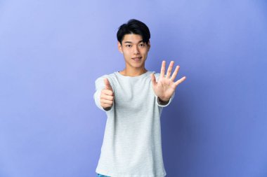 Mor arka planda izole edilmiş genç Çinli adam parmaklarıyla altısını sayıyor.