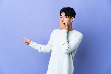 Mor arka planda izole edilmiş genç Çinli bir adam sürpriz bir ifadeyle işaret ederken...