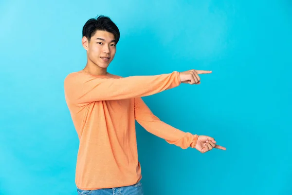 Νεαρός Κινέζος Απομονωμένος Μπλε Φόντο Δείχνοντας Δάχτυλο Στο Πλάι Και — Φωτογραφία Αρχείου