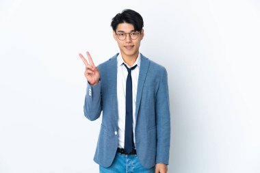 Genç Çinli iş adamı beyaz arka planda izole edilmiş gülümsüyor ve zafer işareti gösteriyor.