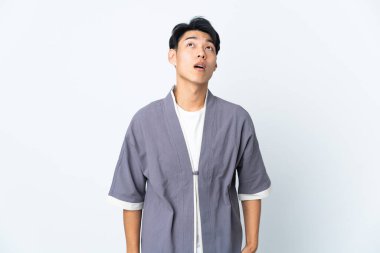 Beyaz arka planda izole edilmiş genç bir Çinli yukarı bakıyor ve şaşırmış bir ifadeyle