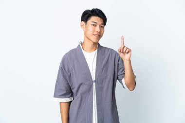 Genç Çinli bir adam beyaz arka planda izole edilmiş ve en iyinin işareti olarak parmağını kaldırıyor.