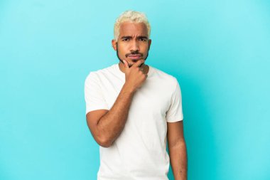 Genç Kolombiyalı yakışıklı adam mavi arka planda soyutlanmış düşünüyor.