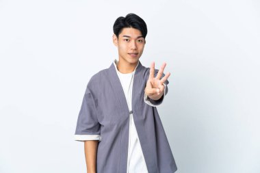 Beyaz arka planda yalnız yaşayan genç bir Çinli mutlu ve parmaklarıyla üçe kadar sayıyor.