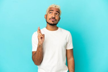 Genç Kolombiyalı yakışıklı adam mavi arka planda izole edilmiş, şans diliyor ve en iyisini diliyor.