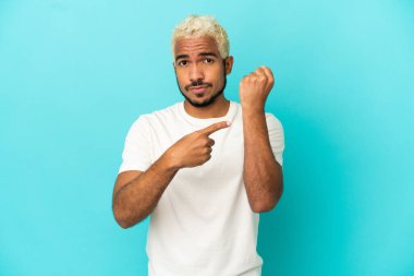 Genç Kolombiyalı yakışıklı adam mavi arka planda izole edilmiş, geç kalma jesti yapıyor.