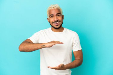 Mavi arka planda izole edilmiş genç Kolombiyalı yakışıklı bir ilan vermek için avucunun içinde hayali bir fotokopi makinesi tutuyor.