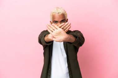 Pembe arka planda izole edilmiş genç Kolombiyalı yakışıklı bir adam bir eylemi durdurmak için elleriyle jesti durduruyor.