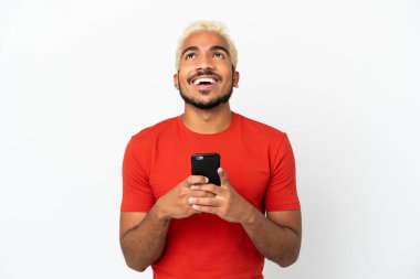 Genç Kolombiyalı yakışıklı adam beyaz arka planda izole edilmiş ve cep telefonu kullanıyor.