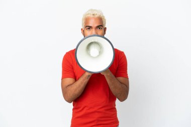 Beyaz arka planda izole edilmiş genç Kolombiyalı yakışıklı bir adam bir şey duyurmak için megafondan bağırıyor.