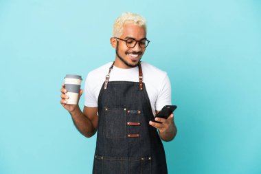 Restoran Kolombiyalı garson mavi arka planda izole edilmiş. Elinde kahve ve cep telefonu var.