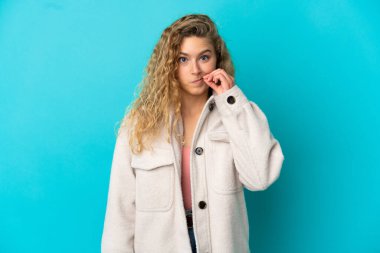 Mavi arka planda izole edilmiş genç sarışın kadın sessizlik işareti gösteriyor.