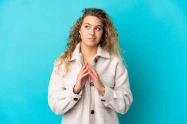 Mavi arka planda izole edilmiş genç sarışın kadın bir şeyler planlıyor.