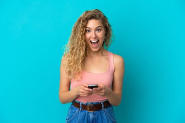 Mavi arka planda izole edilmiş genç sarışın kadın şaşırdı ve bir mesaj gönderiyor.