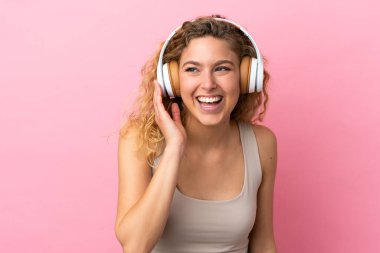 Pembe arka planda izole edilmiş genç sarışın kadın müzik dinliyor.