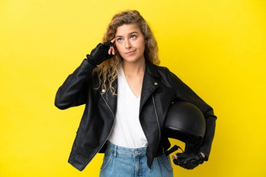 Motosiklet kasklı genç sarışın kadın sarı arka planda izole edilmiş kuşkuları ve düşünceleri var.