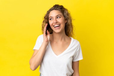 Sarı arka planda izole edilmiş cep telefonu kullanan genç sarışın kadın.