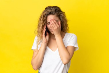 Sarı arka planda izole edilmiş, yorgun ve hasta bir ifadeyle cep telefonu kullanan genç sarışın kadın.