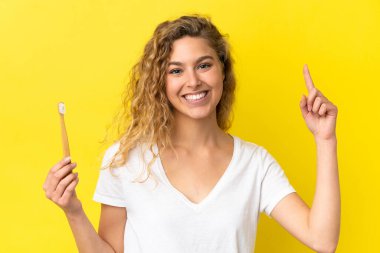 Sarı arka planda diş fırçalayan beyaz bir kadın harika bir fikre işaret ediyor.