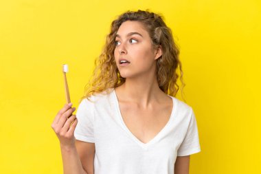 Sarı arka planda dişlerini fırçalayan beyaz bir kadın yan tarafa bakıyor.