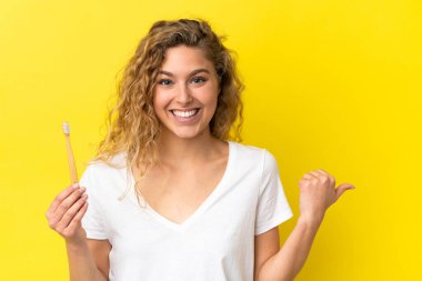 Sarı arka planda dişlerini fırçalayan beyaz bir kadın bir ürün sunmak için yan tarafı işaret ediyor.