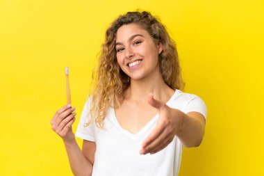 Sarı arka planda izole edilmiş diş fırçalayan beyaz bir kadın iyi bir anlaşma yaptığı için el sıkışıyor.