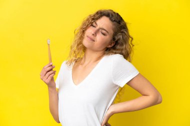 Sarı arka planda dişlerini fırçalayan beyaz bir kadın çaba sarf ettiği için sırt ağrısından muzdarip.