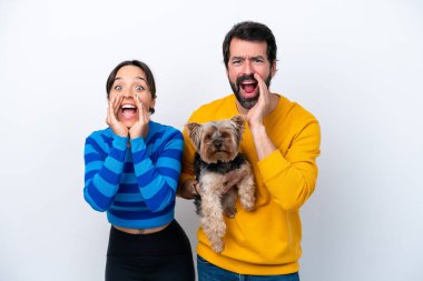 Beyaz arka planda izole edilmiş köpeği tutan genç İspanyol kadın ağzı açık bağırıyor.