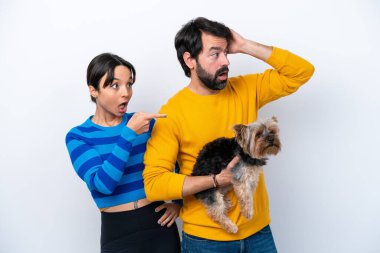 Beyaz arka planda izole edilmiş bir köpeği tutan genç İspanyol kadın şaşırmış bir yüzle parmağını yana gösteriyor.