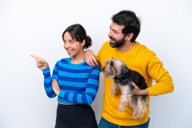 Beyaz arka planda izole edilmiş bir köpeği tutan genç İspanyol kadın bir ürünü sunmak için kenarı işaret ediyor.