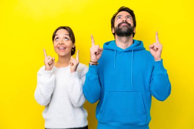 Young caucasian couple isolated on yellow background pointing up with the index finger a great idea