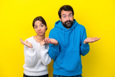 Sarı arka planda izole edilmiş genç beyaz bir çift kuşkuları ve kafa karıştırıcı ifadeleri var.