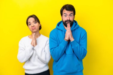 Sarı arka planda izole edilmiş genç beyaz çift yalvarıyor.