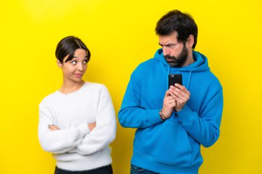 Sarı arka planda izole edilmiş genç beyaz çift cep telefonuyla bir mesaj okuyor.