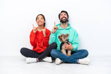 Beyaz arka planda izole edilmiş evcil hayvanlarıyla yerde oturan beyaz bir çift işaret parmağıyla işaret etmek harika bir fikir.