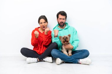 Beyaz arka planda evcil hayvanlarıyla yerde oturan beyaz bir çift zaferi kutluyor.