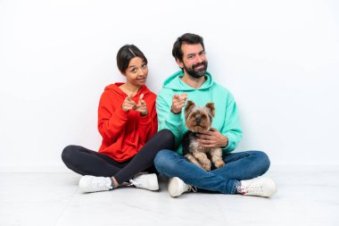 Beyaz arka planda izole edilmiş evcil hayvanlarıyla yerde oturan genç beyaz bir çift sana parmak basıyor.