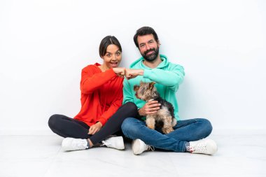 Beyaz arka planda yumruklaşan evcil hayvanlarıyla yerde oturan genç beyaz bir çift.