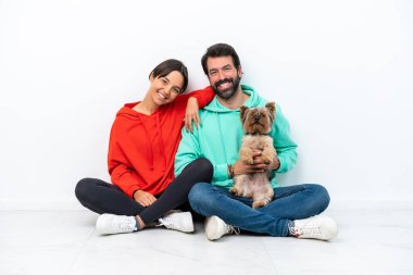 Beyaz arka planda izole edilmiş evcil hayvanlarıyla yerde oturan beyaz bir çift mutlu ve gülüyor.