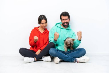 Beyaz arka planda evcil hayvanlarıyla yerde oturan beyaz bir çift galibiyeti kutluyorlar.