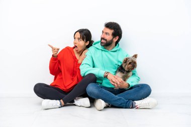 Beyaz arka planda izole edilmiş evcil hayvanlarıyla yerde oturan beyaz bir çift gülümseyerek bir fikir sunuyorlar.