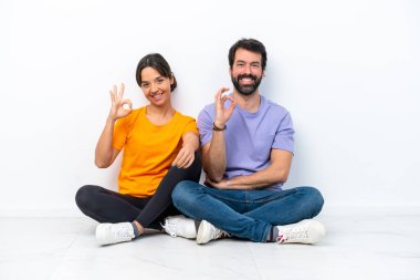 Beyaz arka planda izole bir şekilde yerde oturan beyaz tenli genç çift parmaklarıyla 