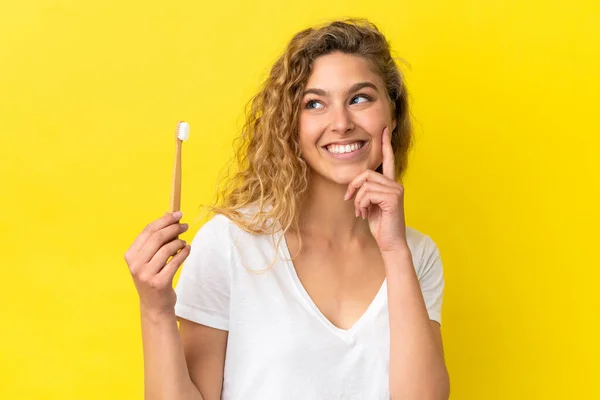 Młoda Biała Kobieta Trzymająca Szczotkujące Zęby Odizolowane Żółtym Tle Myśląc — Zdjęcie stockowe