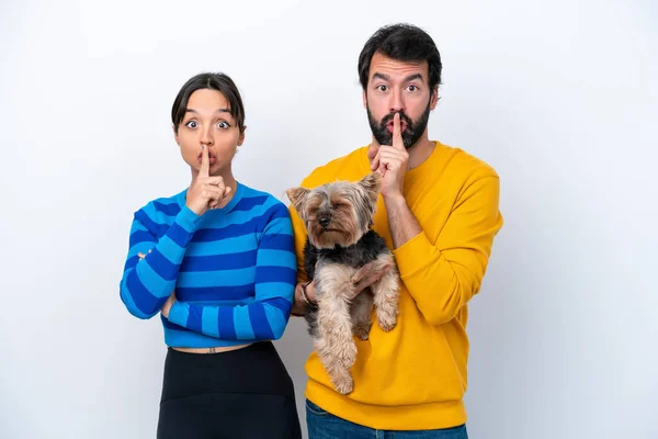 Young hispanic woman holding a dog isolated on white background showing a sign of closing mouth and silence gesture