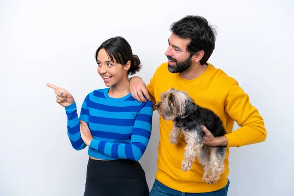 Young hispanic woman holding a dog isolated on white background pointing to the side to present a product