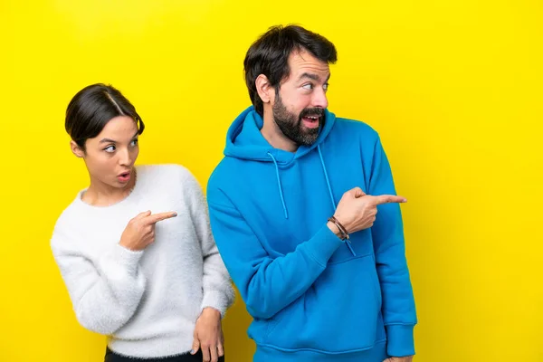 Young Caucasian Couple Isolated Yellow Background Pointing Finger Side Surprised — Foto Stock