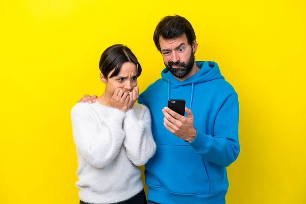 Young Caucasian Couple Isolated Yellow Background Reading Message Mobile —  Fotos de Stock