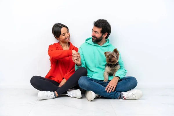 Young caucasian couple sitting on the floor with their pet isolated on white background handshaking after good deal